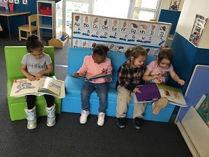 Four preschool students reading on couches