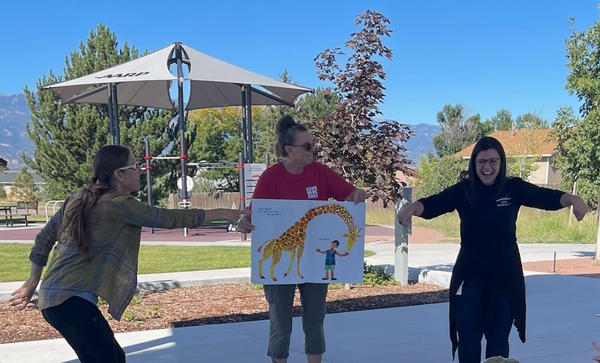 Outside, one woman holds a large book with a picture of a giraffe, while two more women signed the story in ASL.