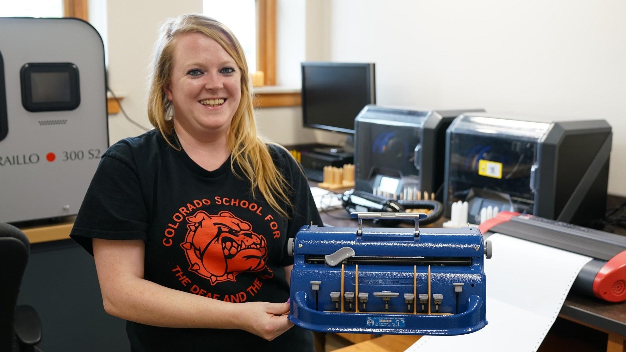 A female staff member holds a brailler with the 3D printed finger guide. 