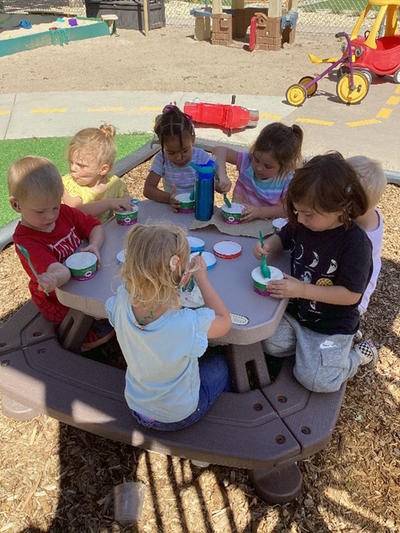 A group of 7 students sit around a table eating a snack.