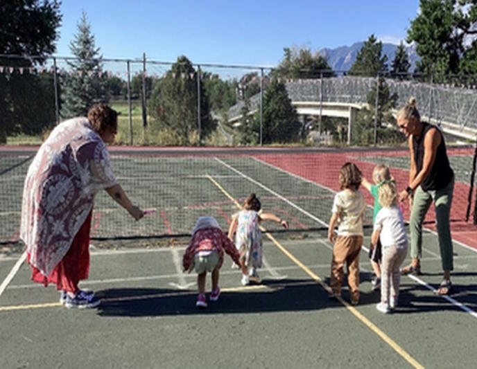 A group of students and two teachers play on the tennis court.