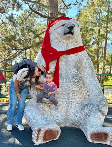 A child sit on a polar bears lap.  Mom stands next to them.