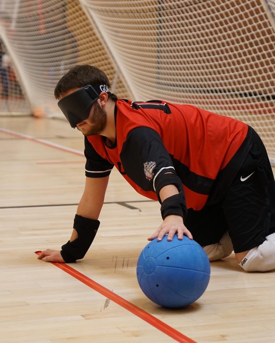 A CSDB on his knees holds a goalball. 