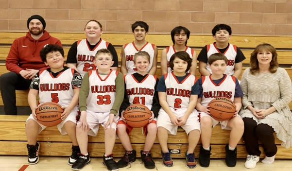 2 rows of boys basketball players and coaches sit on the benches looking at the camera.