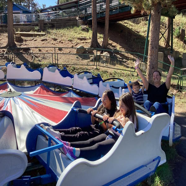 Four people ride a ride, two of them have their hands in the air.