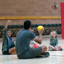 Two students sign the word "yellow" to their teacher, who holds a yellow ball.