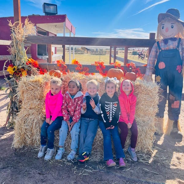 A group of preschool students poses by a hay bale.