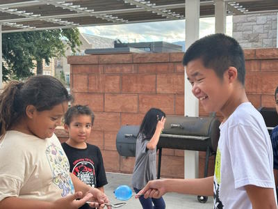 two students passing a water balloon back and forth with a spoon.  Two others students watch.