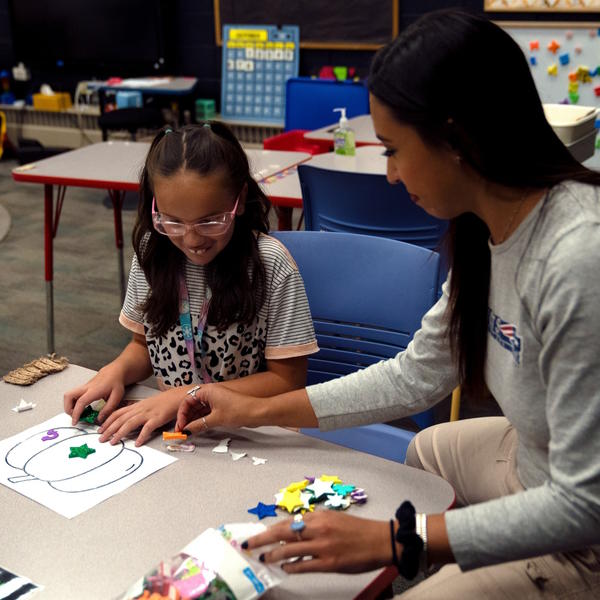 A teacher helps a student choose stickers for her pumpkin. 