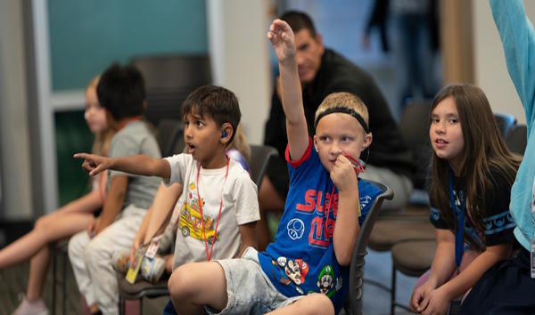 A boy raises his hand, another boy points to the front of the room.