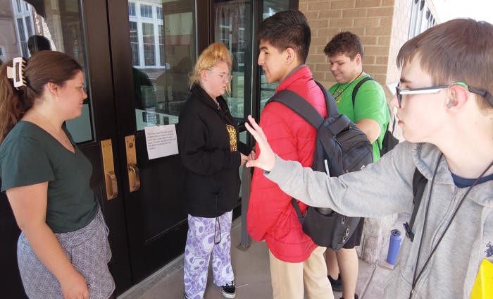 Students and teacher stand outside a building door with a clue for the scavenger hunt.