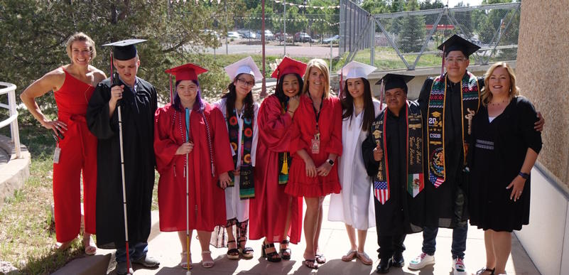 Seven student graduates wearing red, white and black cap and gowns, standing with three staff members.