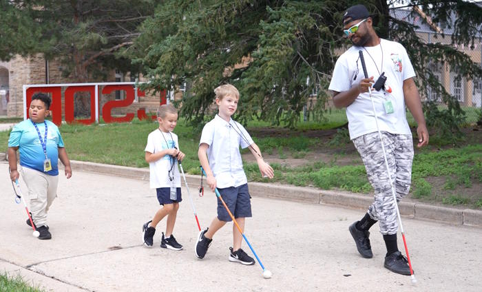 a teacher and three students walk in a line with their canes.