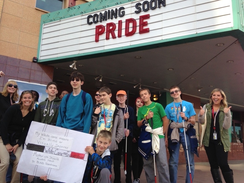 Blind student group on white cane day in front of cinema marquee "Pride"