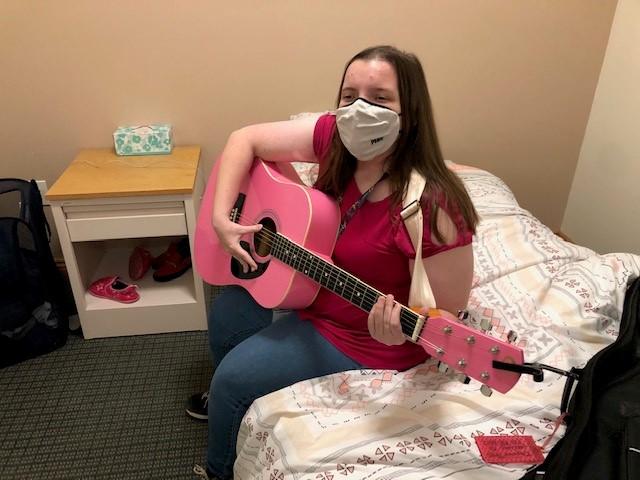 Student plays her pink guitar in her dorm room.