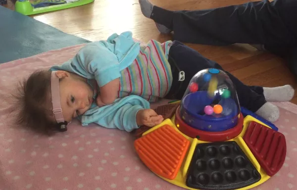 infant wearing a LENA device playing with a musical toy