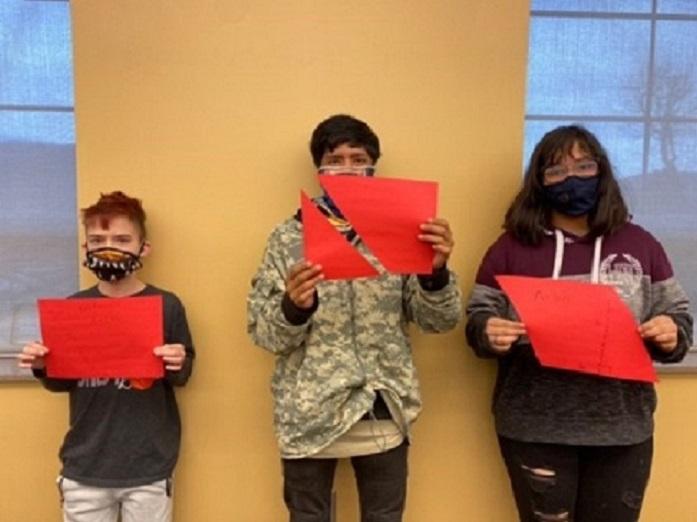 Three students hold geometric paper shapes