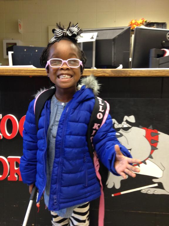 An elementary student smiles while standing by the School for the Blind front desk.