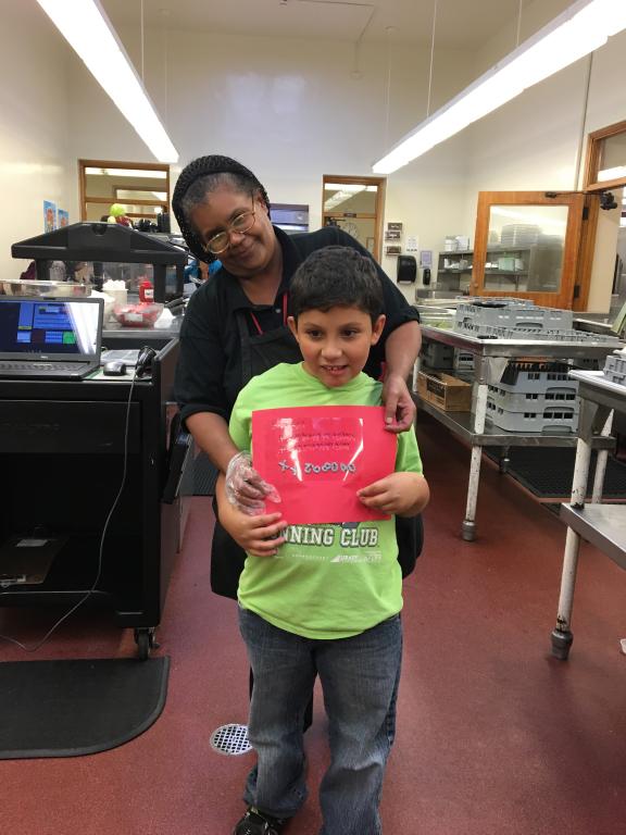  A student poses with one of our cafeteria staff holding a card that he made for her.