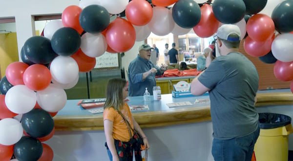 two people stand in front of concession count and a balloon arch talking to a man behind the counter.