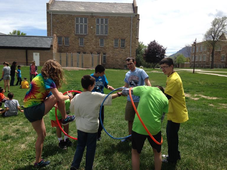 Students and staff participate in a yard activity by passing a hula hoop around their circle while holding hands.