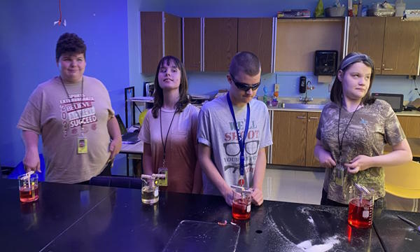 Four students standing at a table with glass beakers of fluid used to make rock candy.
