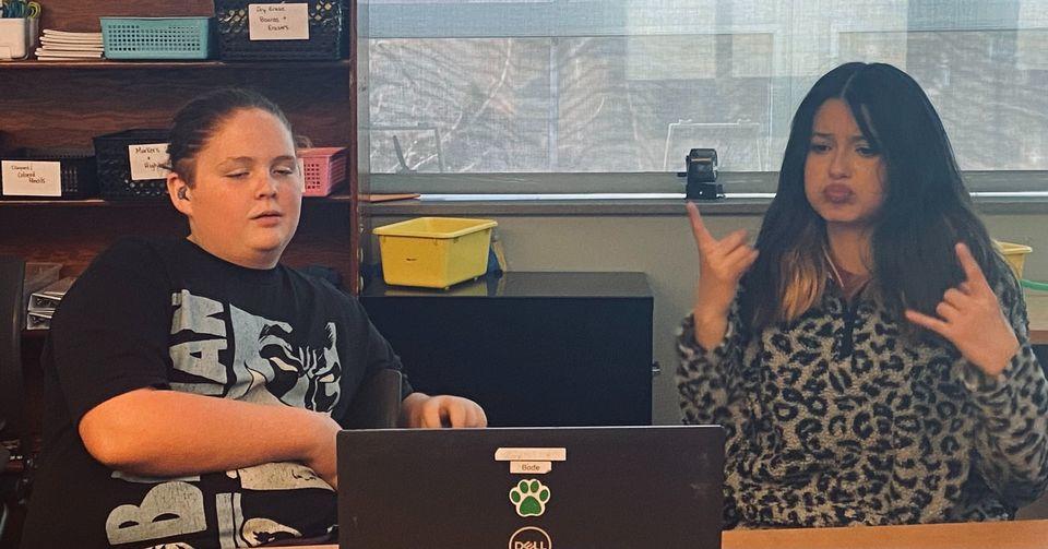 A male and female student, who is using ASL, working with a laptop in a classroom.]