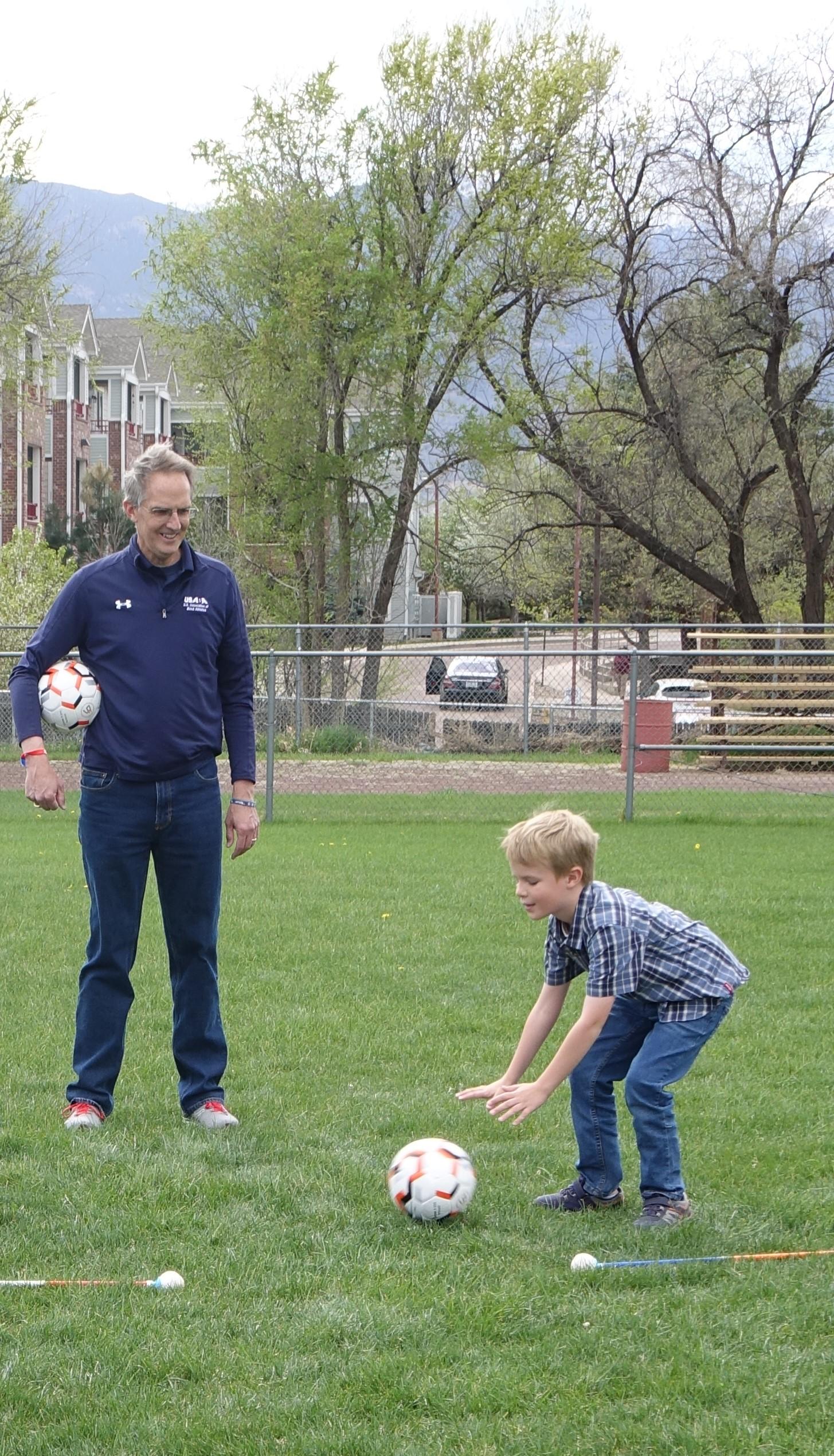 Man holds soccer ball while a boy puts a soccer ball on the ground