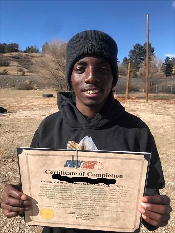 Man dressed in a black hoodie and beanie standing outside holding a certificate of completion of the CDL course.