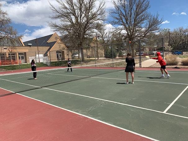 Two teams of two students play pickleball on the tennis court