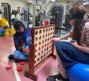 two players sit across from each other on their own side of the Connect 4 board