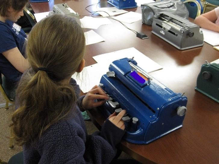 Alt text: A student is brailling her contest answers using an APH Light Touch brailler during the Denver Braille Challenge contest.