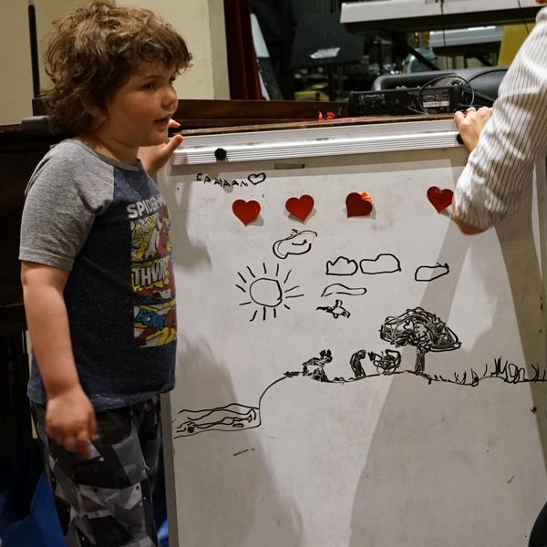 Student stands next to a large piece of white page with drawings four heart stickers.