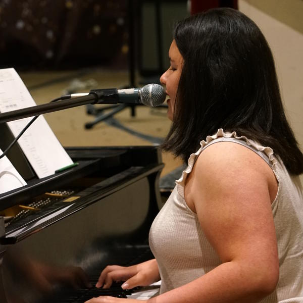 Student plays the piano and sings into a microphone.