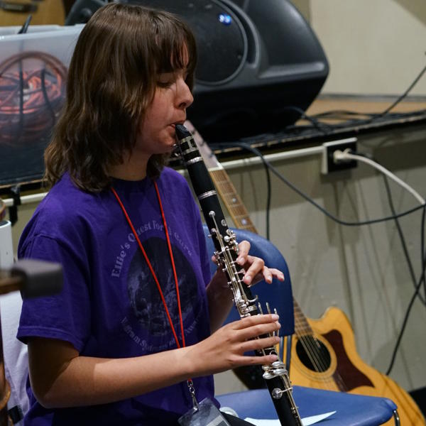 Student sits in a chair and plays the clarinet.