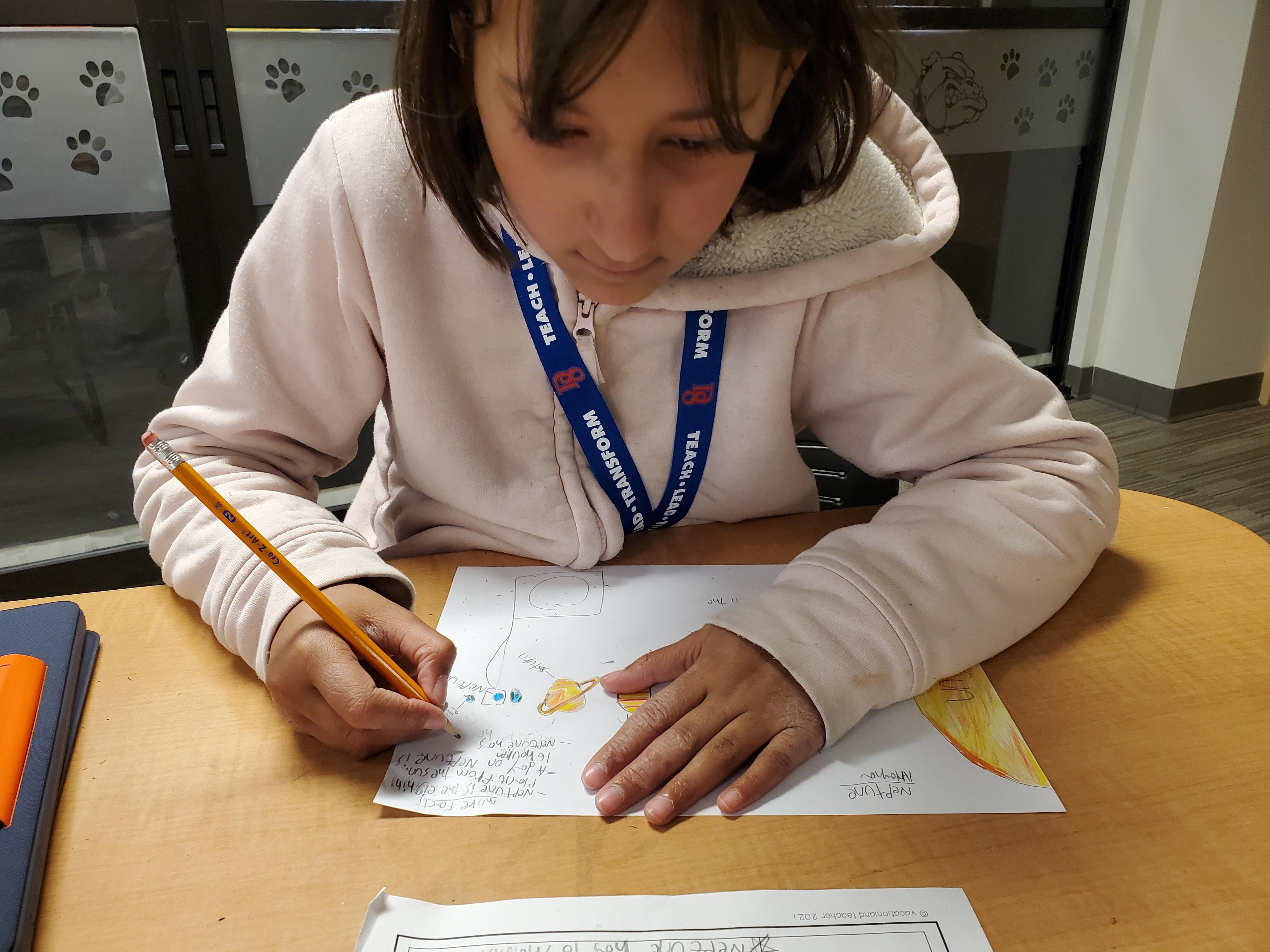 Girl uses pencil to write at her desk