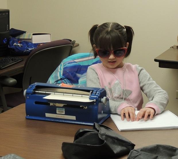 Young girl reads a braille sheet next to her brailler