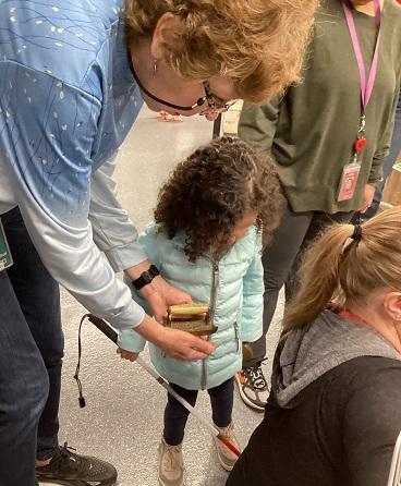 Female teacher holds old iron for preschool girl who is blind