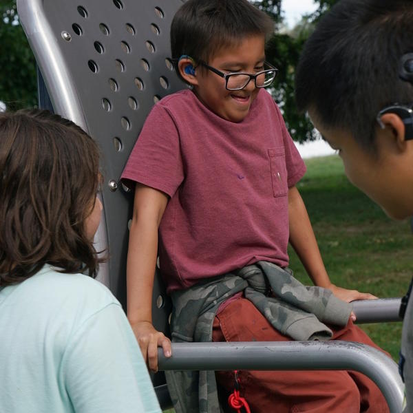 Student wearing glasses plays on playground, while other students watch.