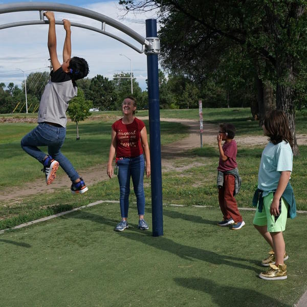 Student plays on playground equipment, while teacher and two other students watch student.