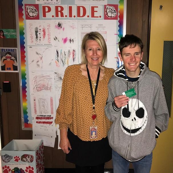 Caption: Student, who won September’s PRIDE Award, standing with his teacher who nominated him. Both have beaming smiles on their faces.