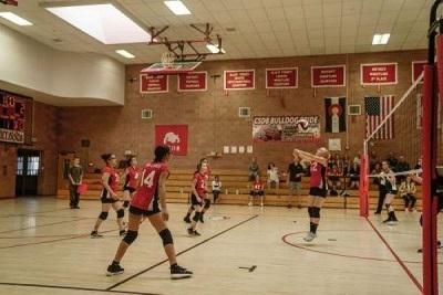 Athletes playing volleyball at a girls high school game, one player is getting ready to hit the ball over the net.
