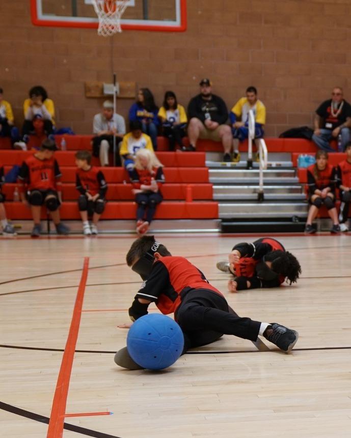 A CSDB student lies on the court, stopping a goalball with his foot. 