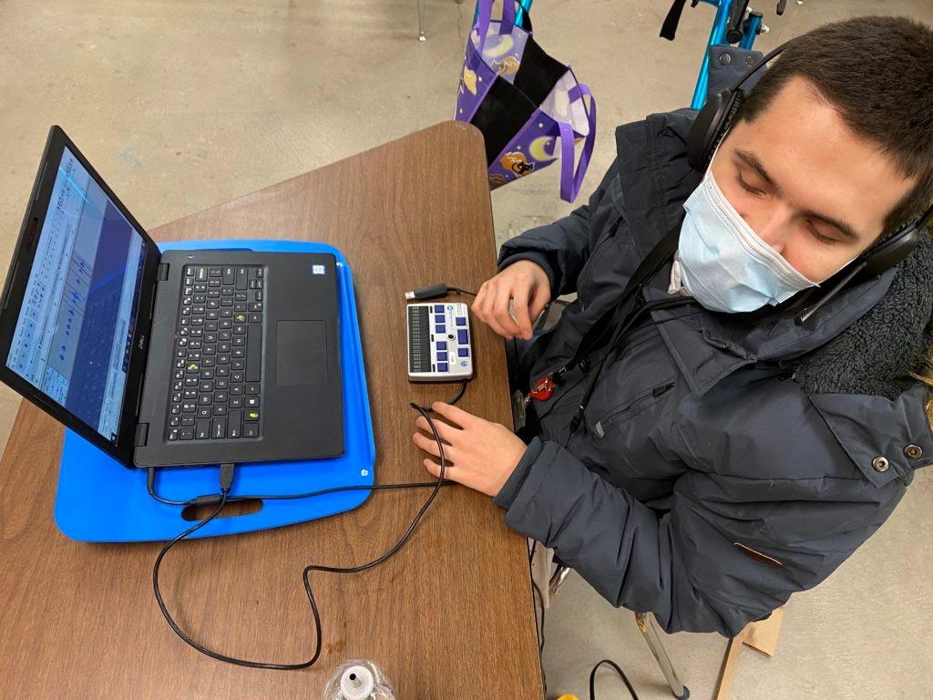 Male student works with braille device connected to his laptop