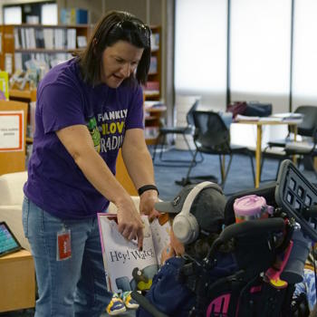 A librarian holds a book close to a student, so she can look at a page.