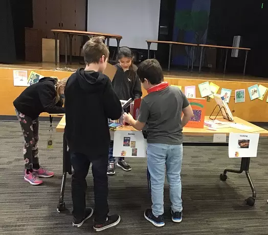 our students look through books displayed on a table; two students write pages under the book table.