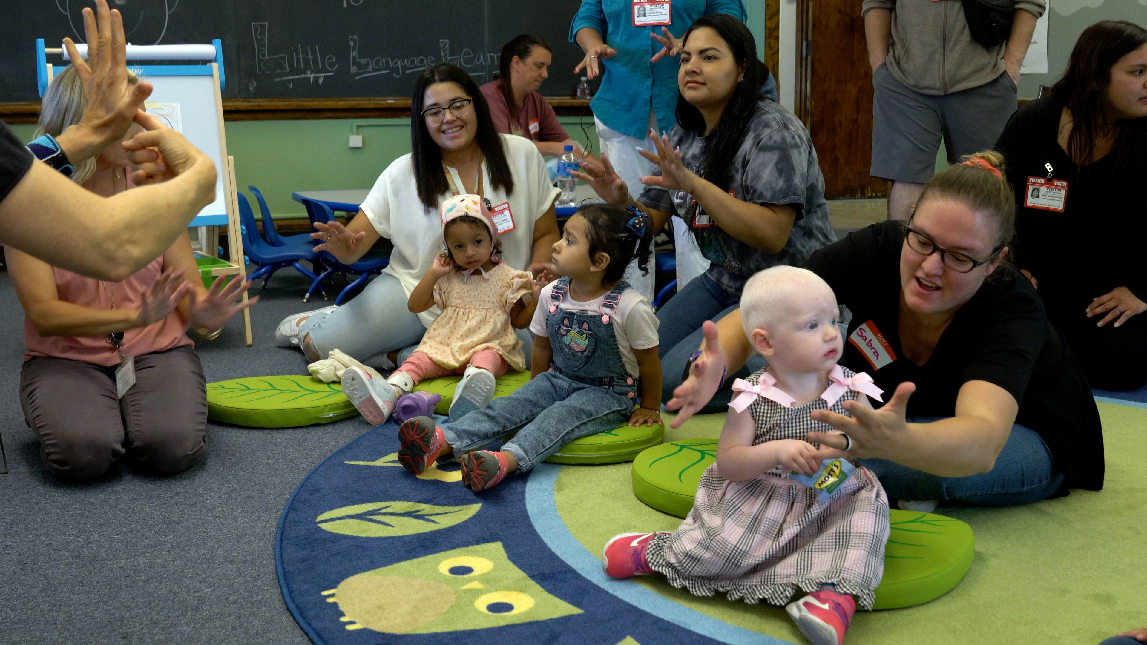 Three small children and their families sit on the floor together