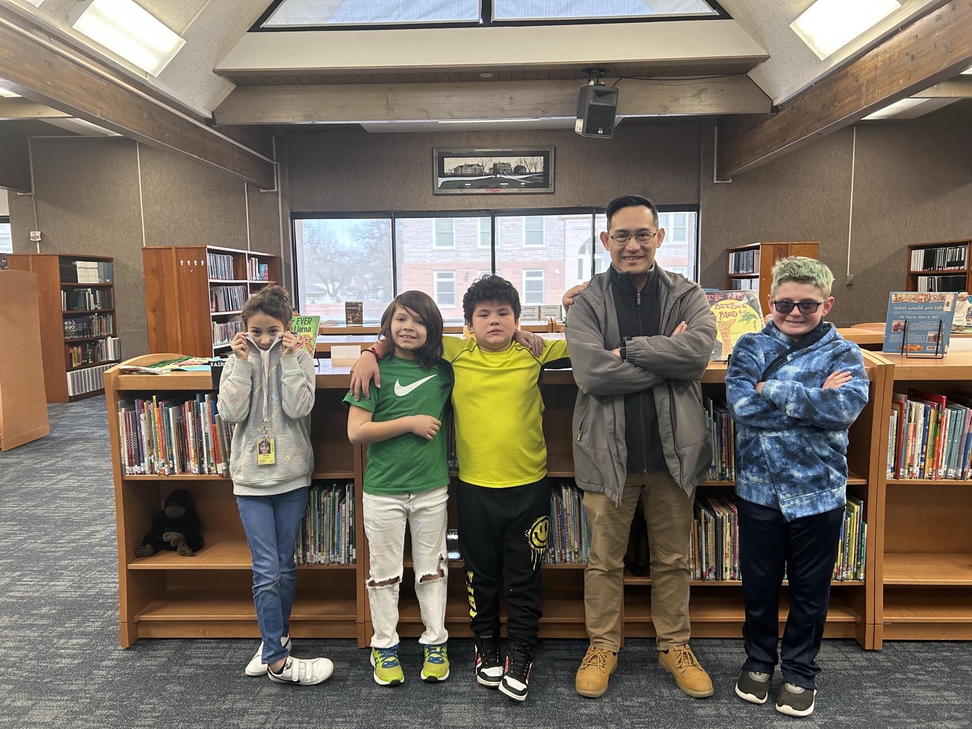 3 boys and a girl stand with a teacher in the library