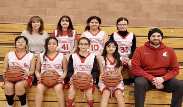 2 rows of girls basketball players and coaches sit on the benches looking at the camera.