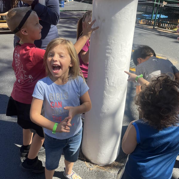 A student smiles at the camera, while other students play behind.